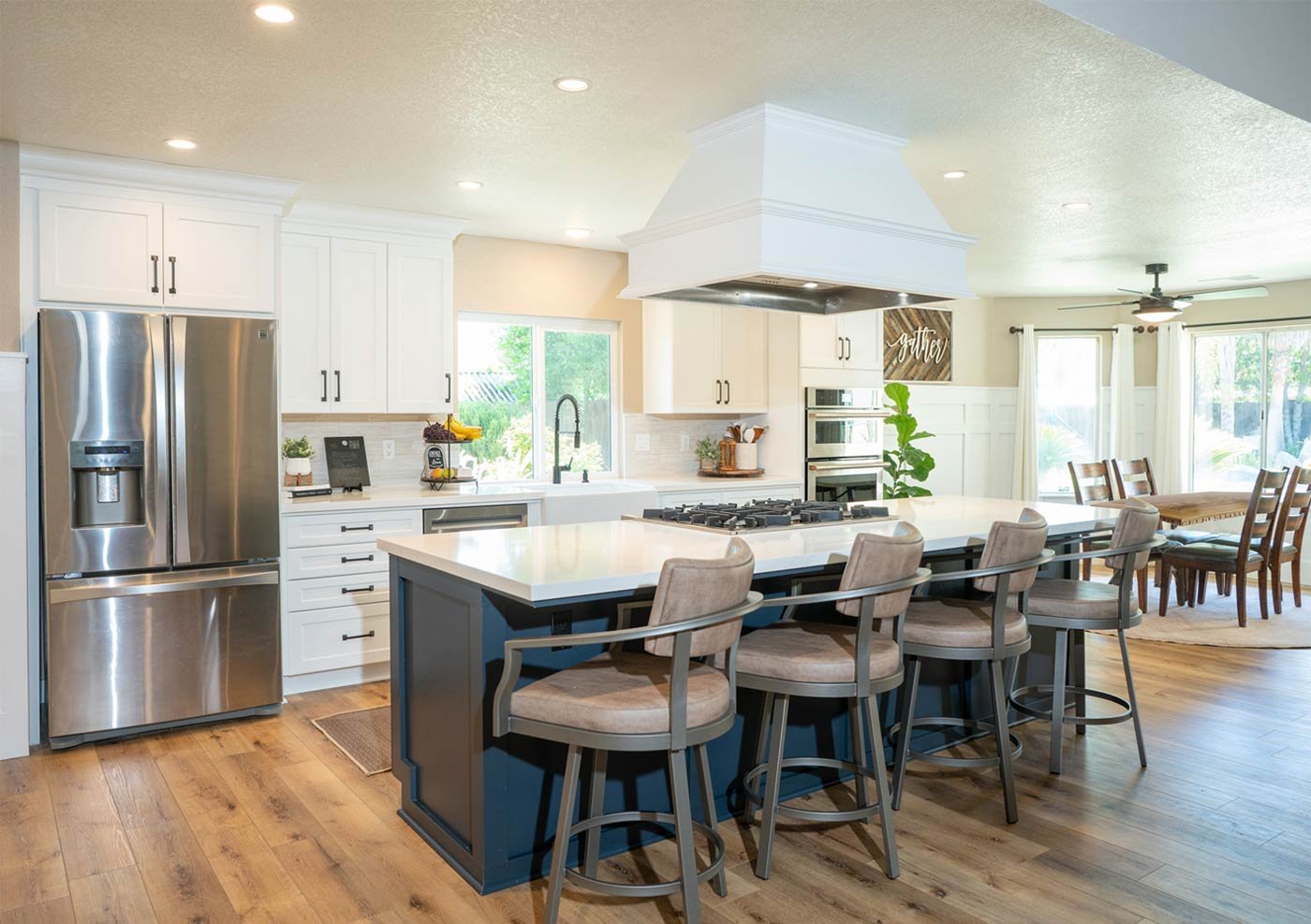 Bright open-concept kitchen in Fresno remodeled by Imagine Remodeling featuring white cabinets, blue island, and wood floors