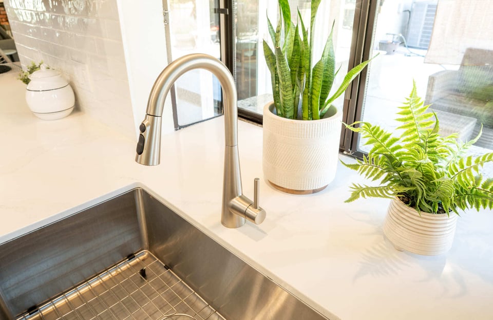 Close-up of modern kitchen sink with stainless faucet, quartz counter, and potted plants in Fresno, CA