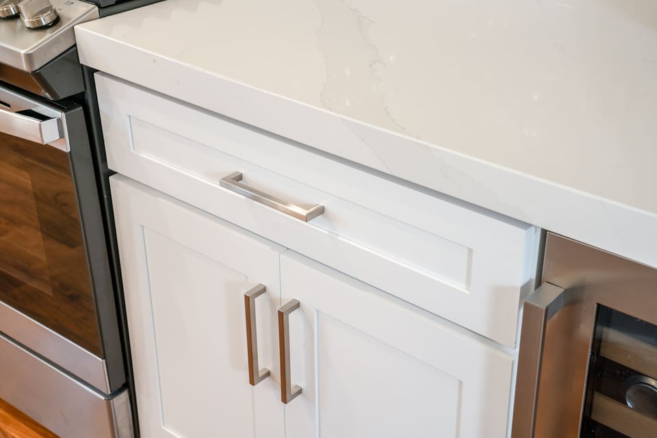 Close-up of white kitchen cabinets with brushed metal hardware and quartz countertop in a Fresno, CA home