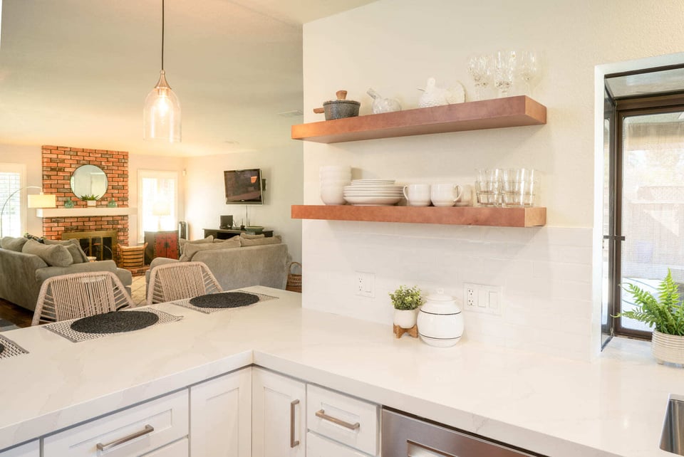 White kitchen with floating wood shelves, quartz countertops, and open view to living area in Fresno, CA