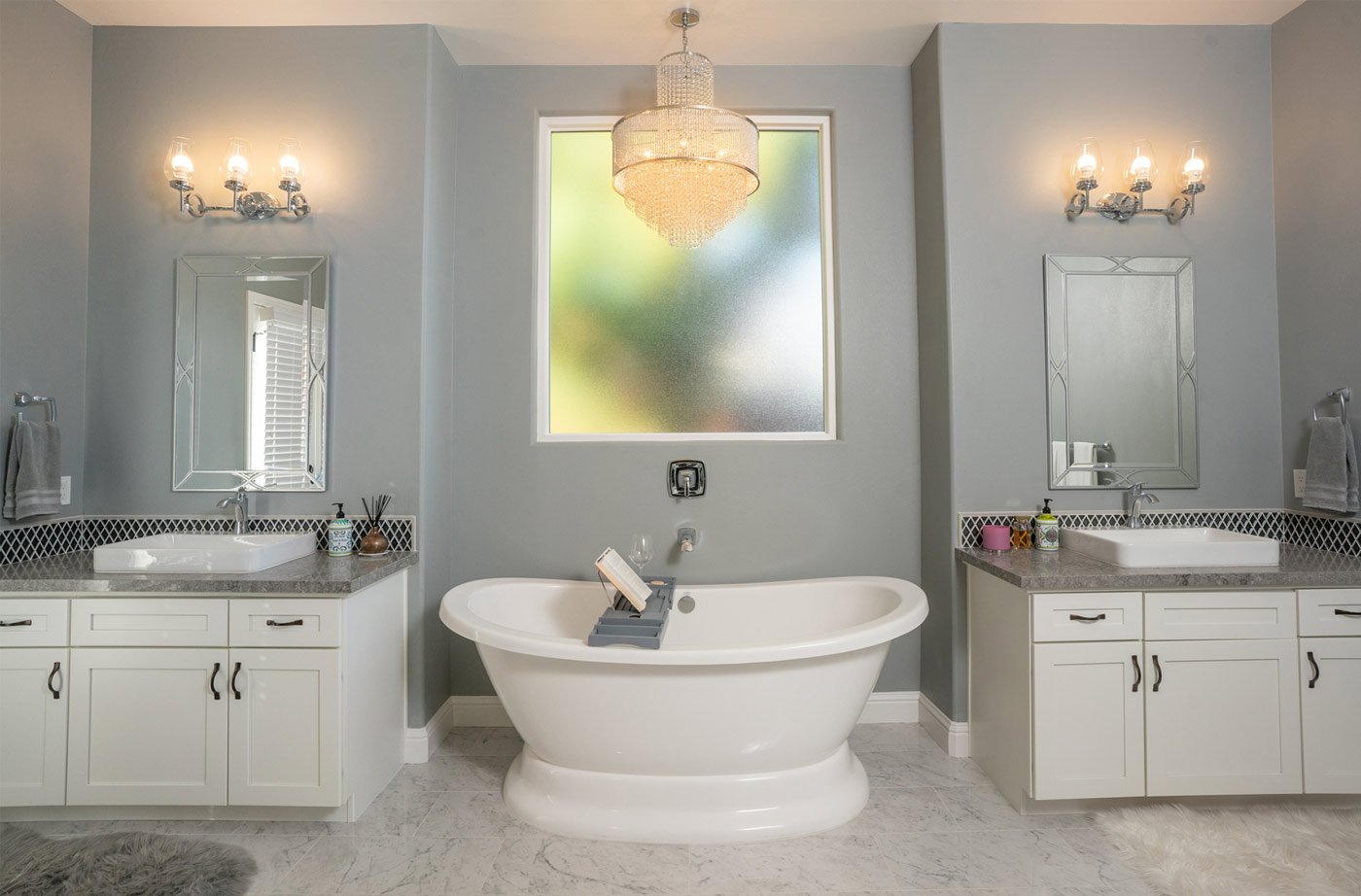 Modern gray and white bathroom with freestanding tub in Fresno, CA, featuring dual vanities and chandelier
