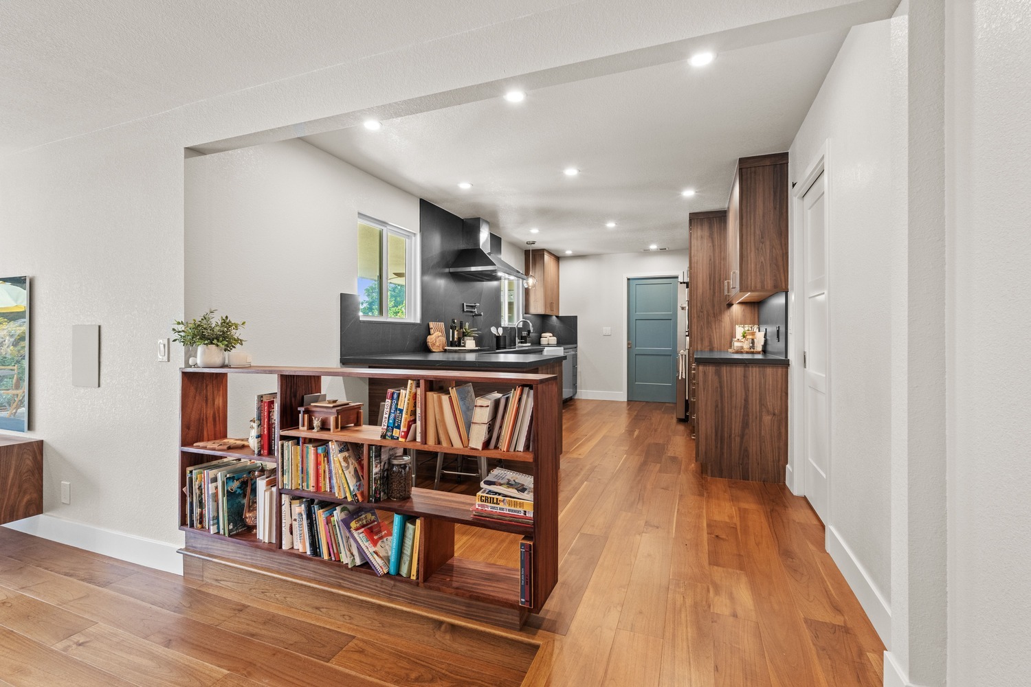 Open Fresno kitchen with wood floors, bookcase divider, and dark stone accents