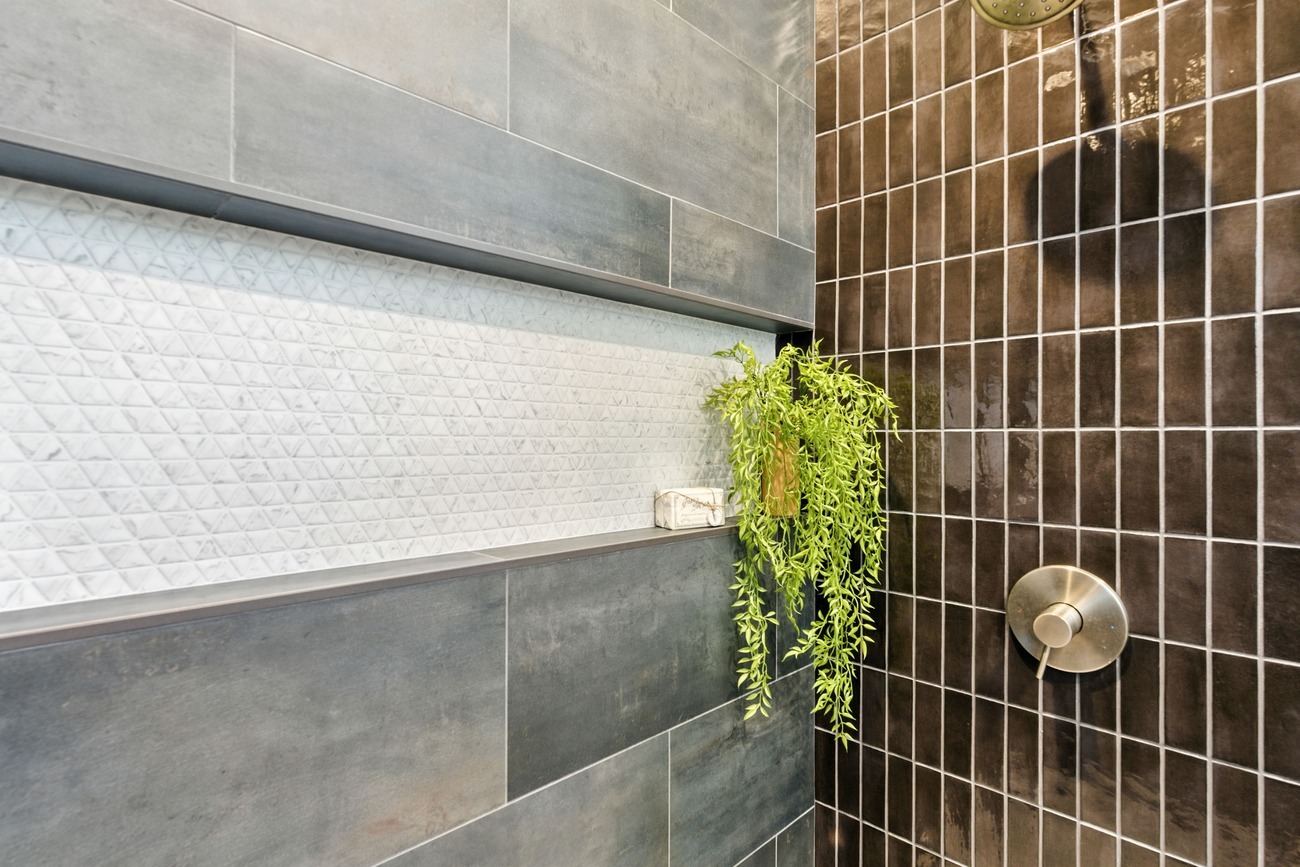Fresno shower close up with dark tile, white niche shelf, and cascading green plant