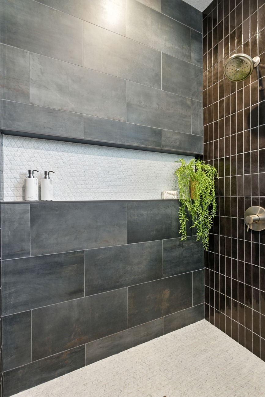 Fresno shower with dark tile walls, white niche shelf, rainfall shower head, and hanging greenery
