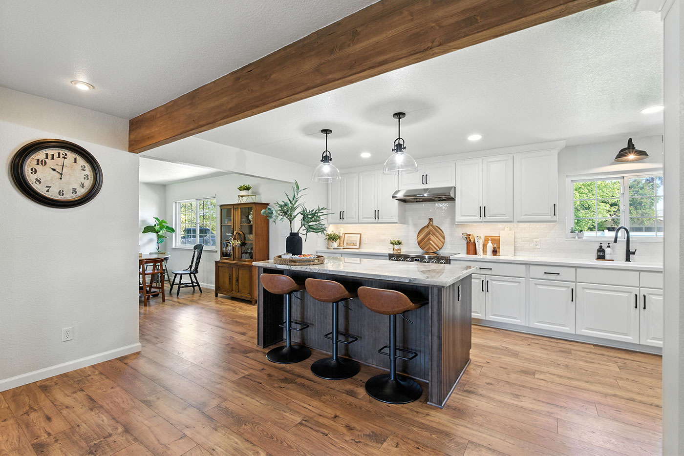 Open-concept Clovis kitchen remodeled by Imagine Remodeling with white cabinets, wood floors, and a marble island with bar seating Open-concept Clovis kitchen remodeled by Imagine Remodeling with white cabinets, wood floors, and a marble island with bar seating